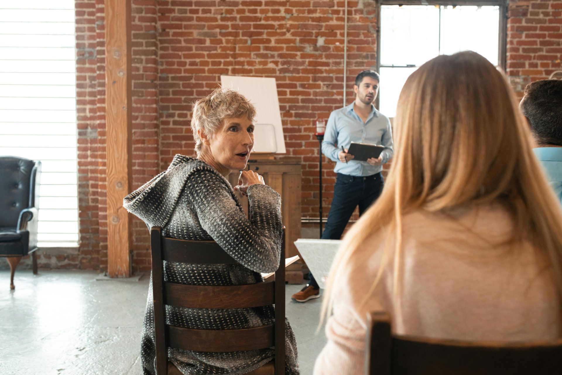 Group of adults engaged in a seminar in a rustic setting with brick walls and wooden chairs.