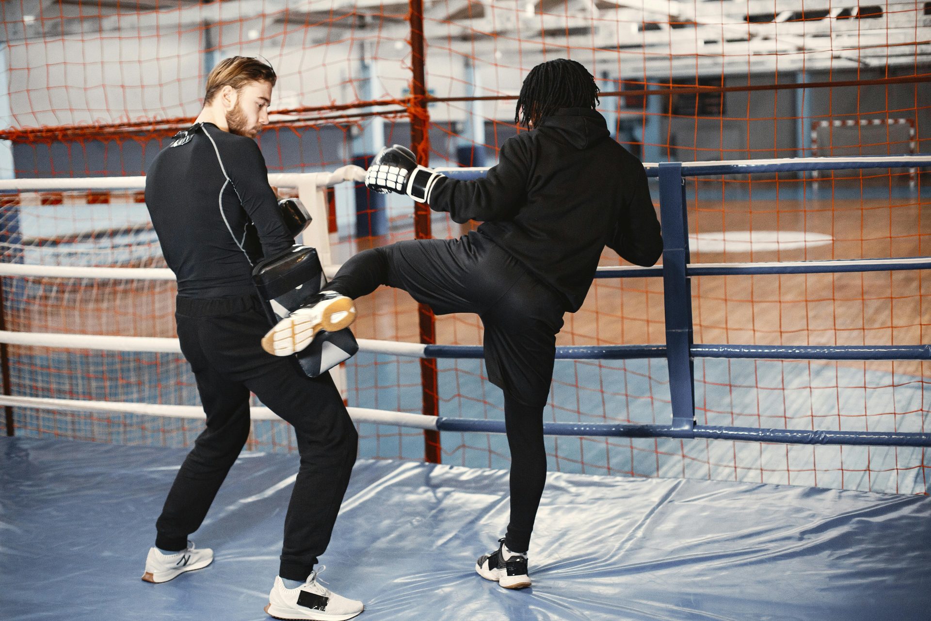 Two men practicing kickboxing in an indoor boxing ring, focusing on high-energy training and technique.
