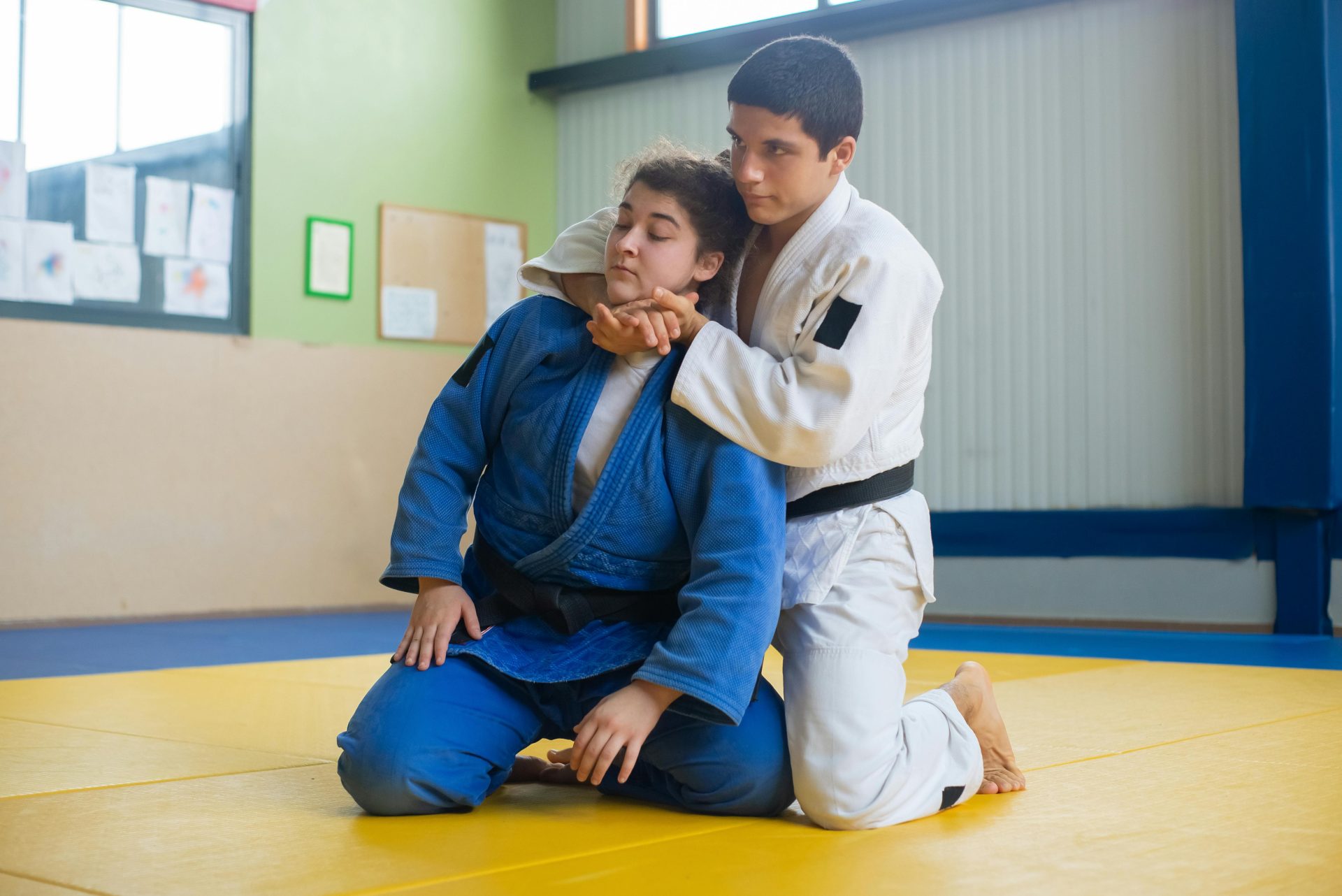 Two judokas engaged in a judo training session on a dojo mat indoors, showcasing grappling techniques.