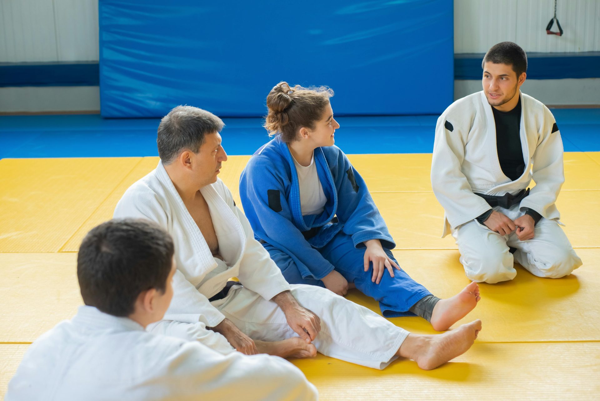 Martial arts class with adults discussing techniques in judo uniforms on mats.